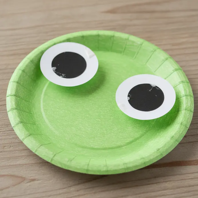 A green paper plate frog with large white and black paper eyes on the top.