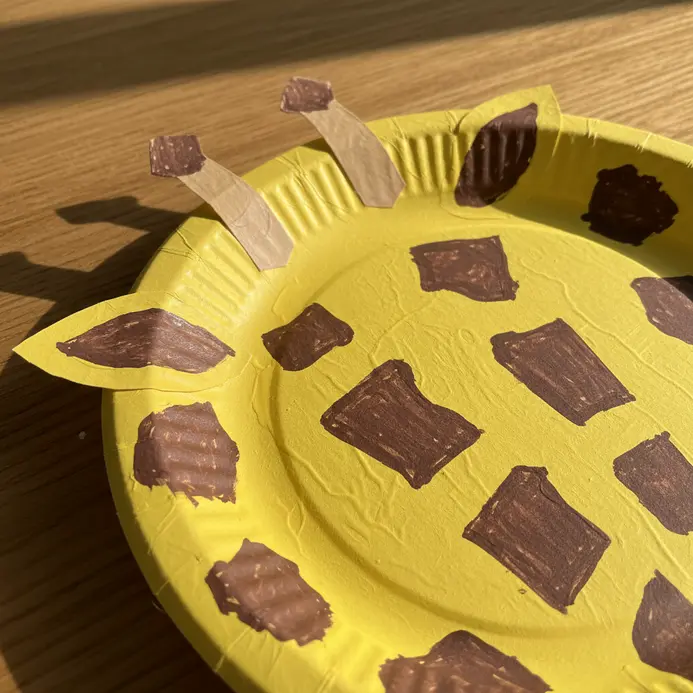 A yellow paper plate giraffe head with brown paper spots and small ossicones on top.