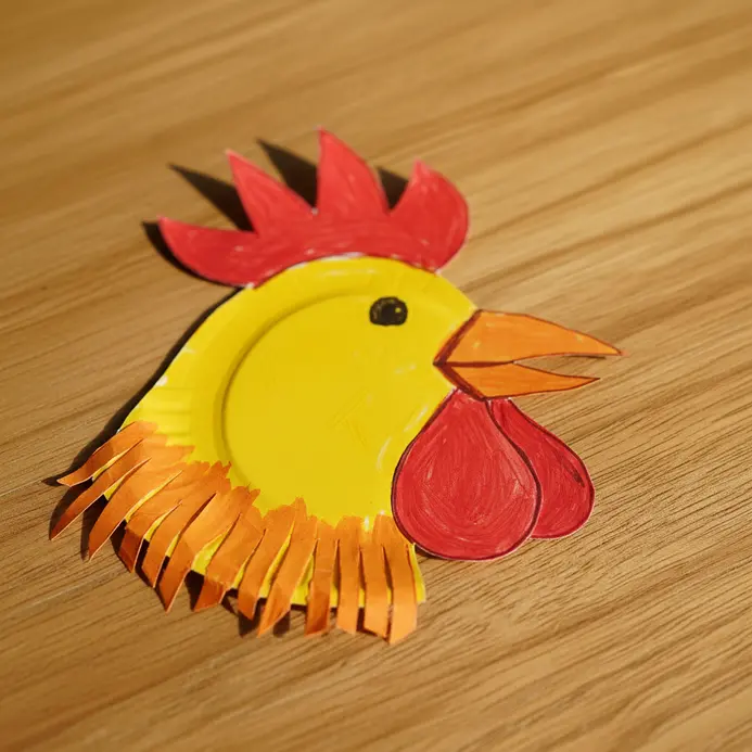A yellow paper plate rooster with a red paper comb, orange beak, and googly eyes.