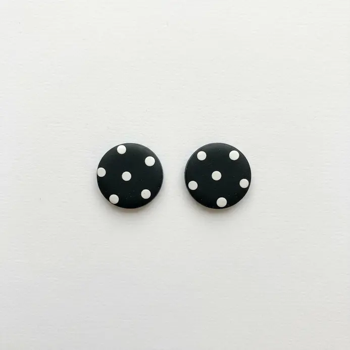 Two flat, black circular stud earrings decorated with evenly spaced white clay dots.