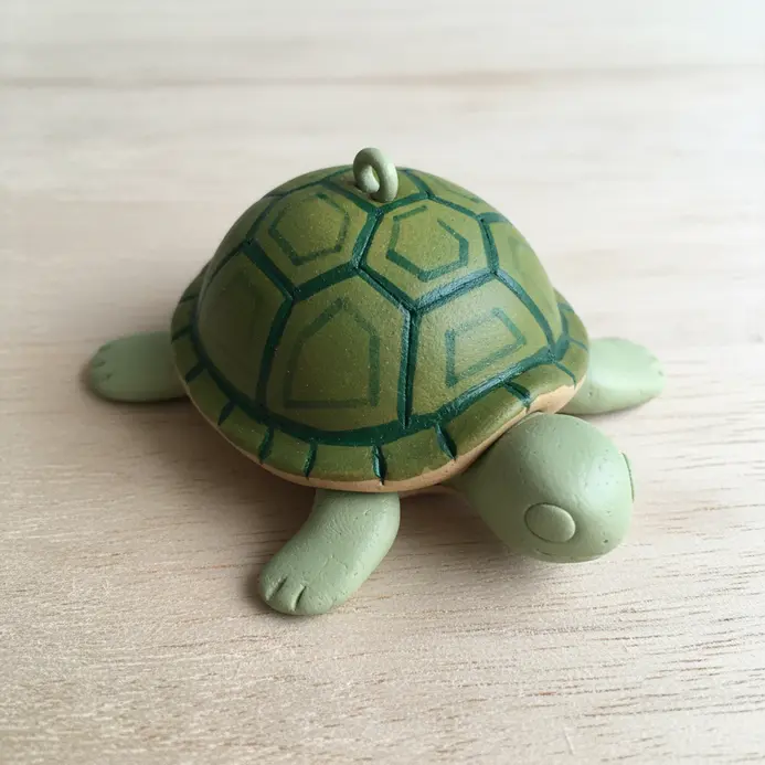 A small turtle with a textured green shell, a head, and four legs, attached to a keyring.