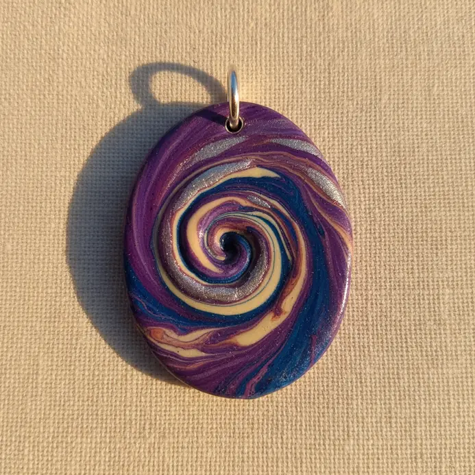 An oval pendant showing a smooth blend of purple, blue, and silver clay in a swirling pattern.