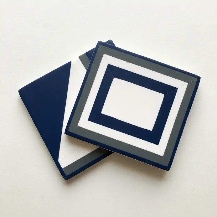 Two square coasters made from layered clay in blue and white, forming simple geometric patterns.