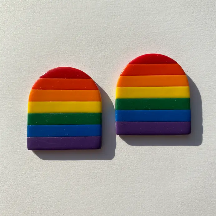 Two thin, arched earrings showing stripes of red, orange, yellow, green, blue, and purple clay.