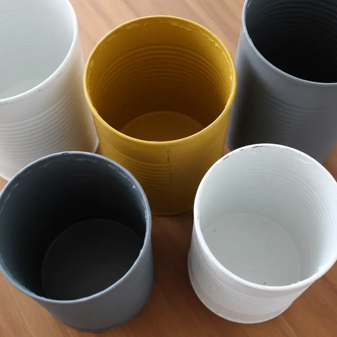 Several clean tin cans painted in a cohesive color scheme, used to organize cooking tools.