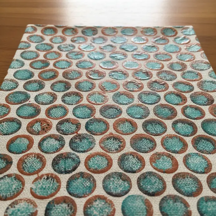 A canvas artwork featuring a repeating circular texture achieved by painting over pressed bubble wrap.