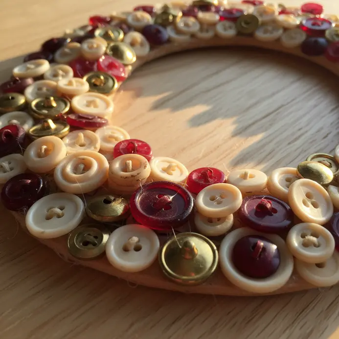 A wooden picture frame embellished with a colorful design made by gluing assorted buttons around its edges.