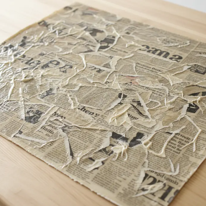 A textured canvas artwork created by collaging and sealing pieces of newspaper.