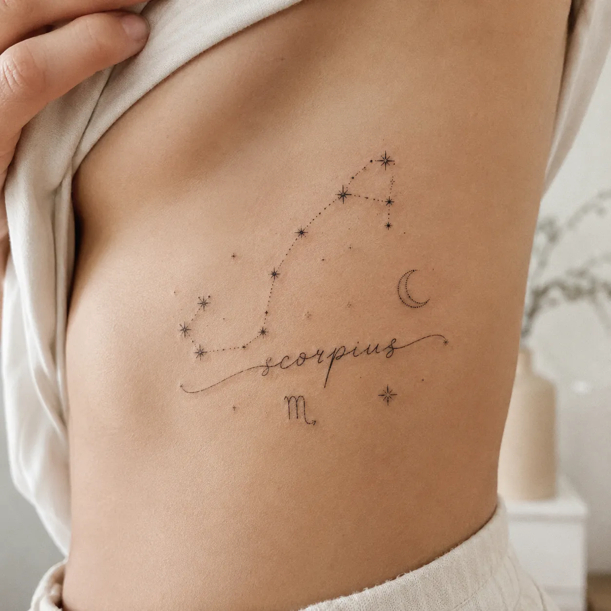 A hand-poked tattoo on the ribcage showing the Scorpius constellation alongside flowing script lettering in a celestial theme.