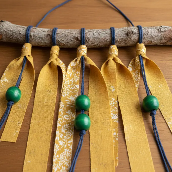 A forked tree branch hangs with strips of patterned fabric and wooden beads.