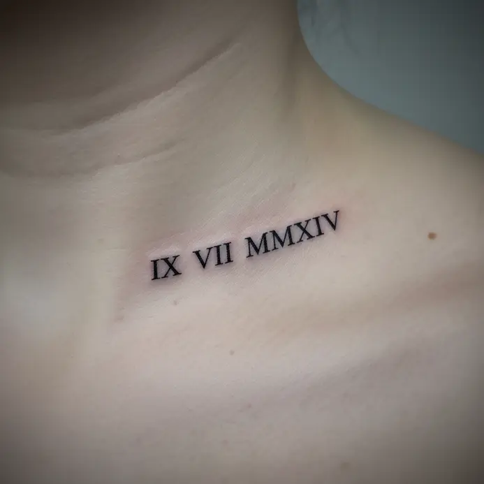 A minimalist tattoo of a significant date rendered in Roman numerals along the collarbone.