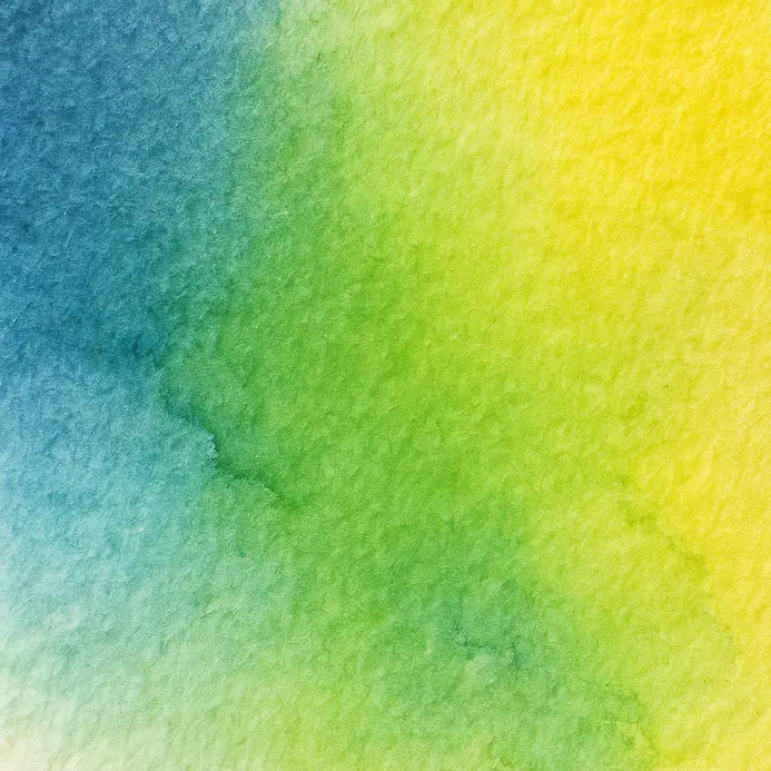 A brush mixes blue and yellow watercolor to create a green shade on a palette.