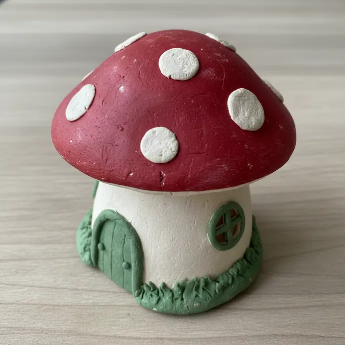 A red and white polymer clay toadstool with a painted door at its base.