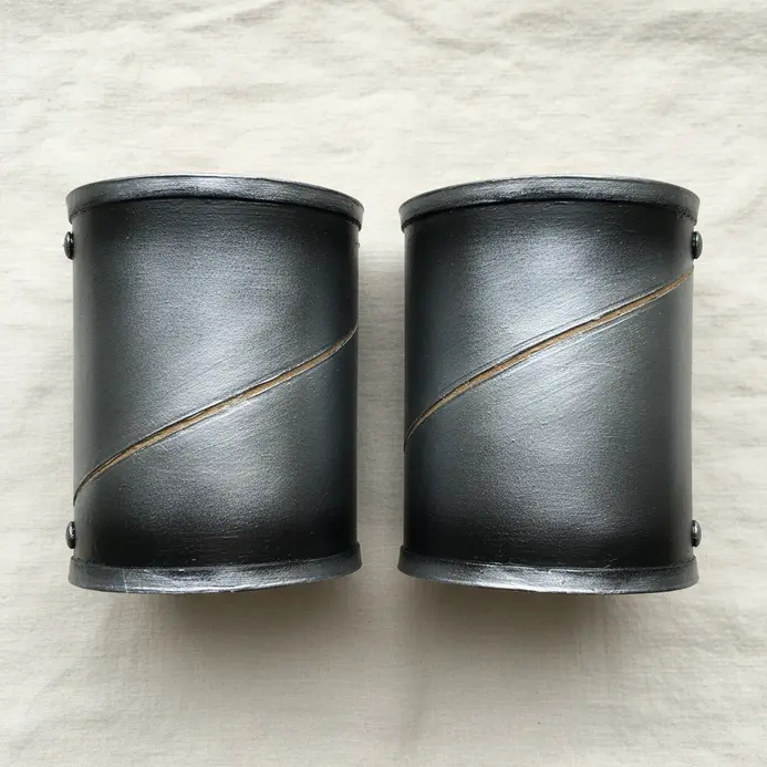 Two cardboard tubes painted silver and gray to resemble medieval armor cuffs.