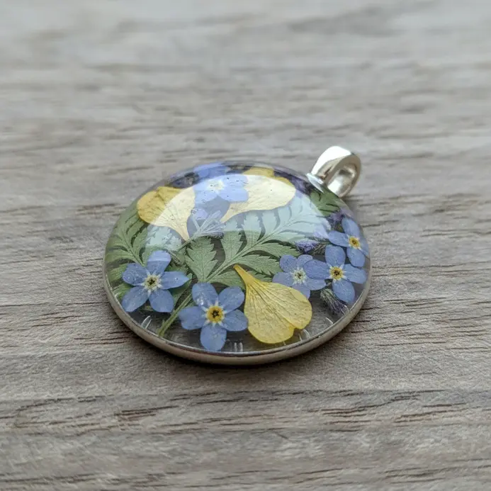 A clear glass cabochon pendant showing delicate pressed forget-me-not flowers inside.