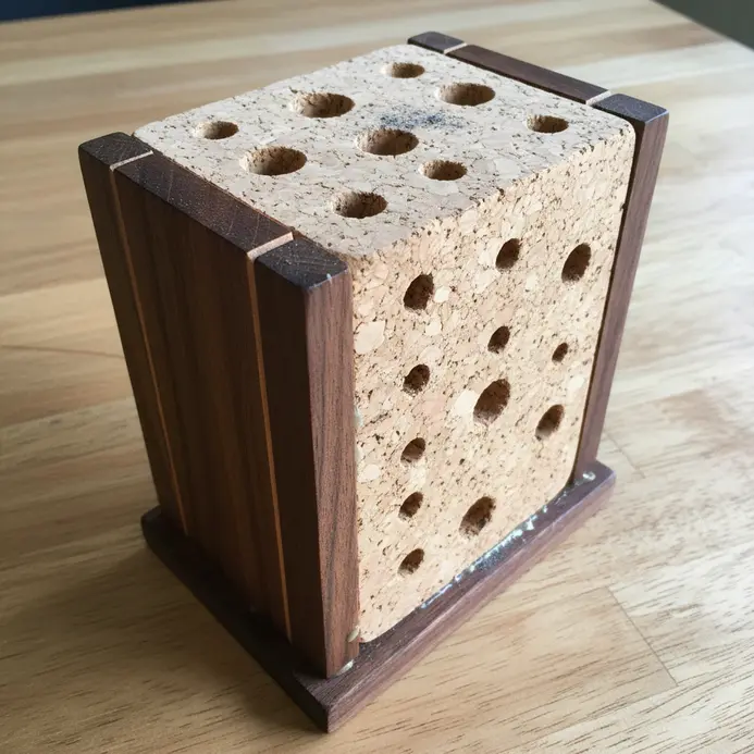 A vertical block made from glued wine corks with holes drilled to hold pencils and pens on a desk.