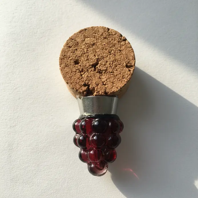 A reusable bottle stopper with a decorative top made from a sliced wine cork round and a metal clasp.