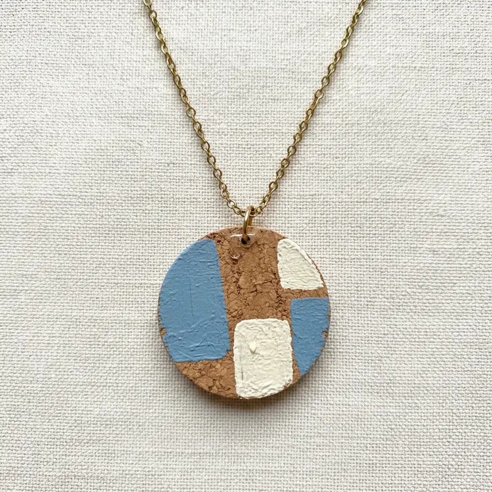 A delicate necklace with a small, painted wine cork slice as a pendant on a thin chain.