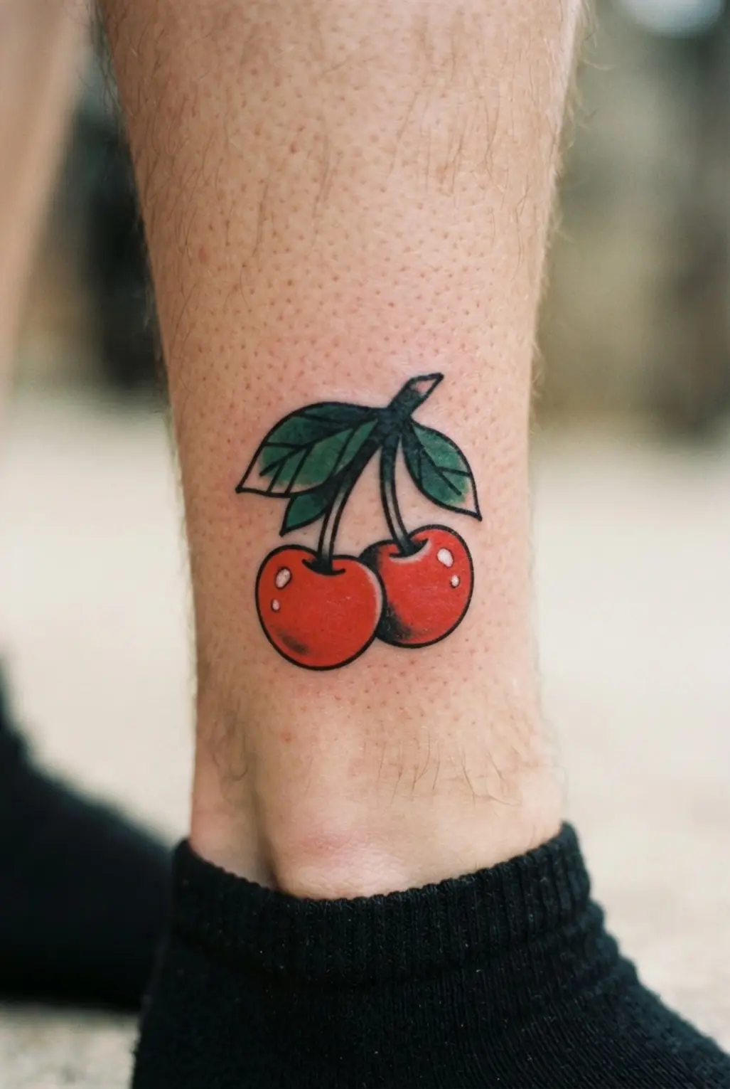 Two red cherries with green leaves on the shin, framed by thick black outlines and small highlights.