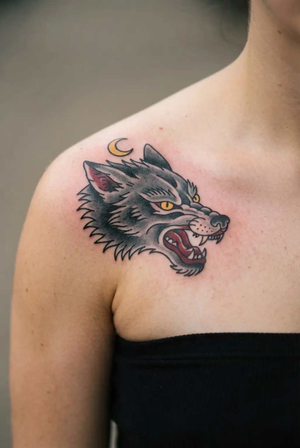 Traditional wolf head chest tattoo with gray fur, red mouth, yellow eyes, and a small crescent moon.