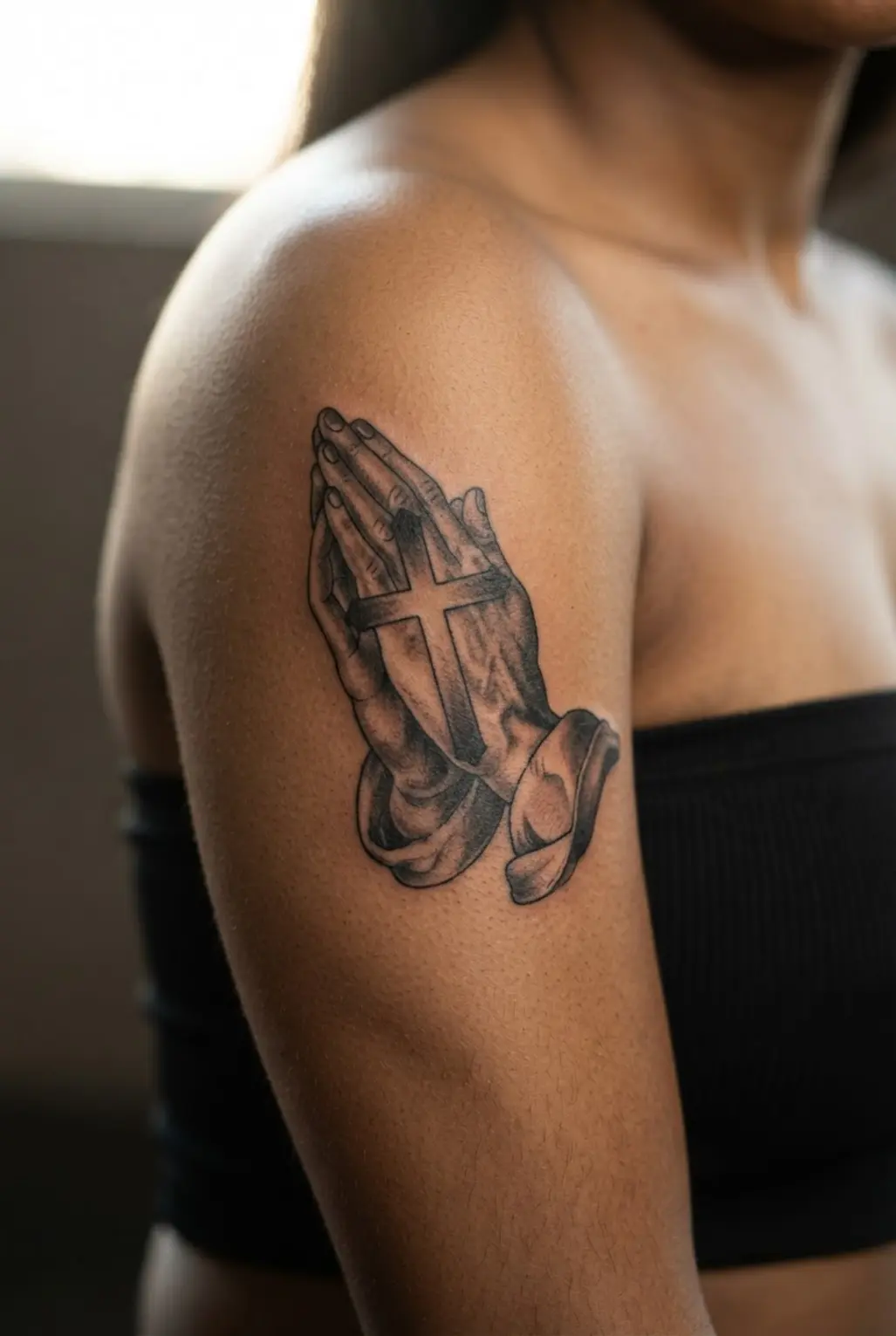 Two praying hands frame an interlocking cross on the bicep with detailed fingers and balanced black shading.