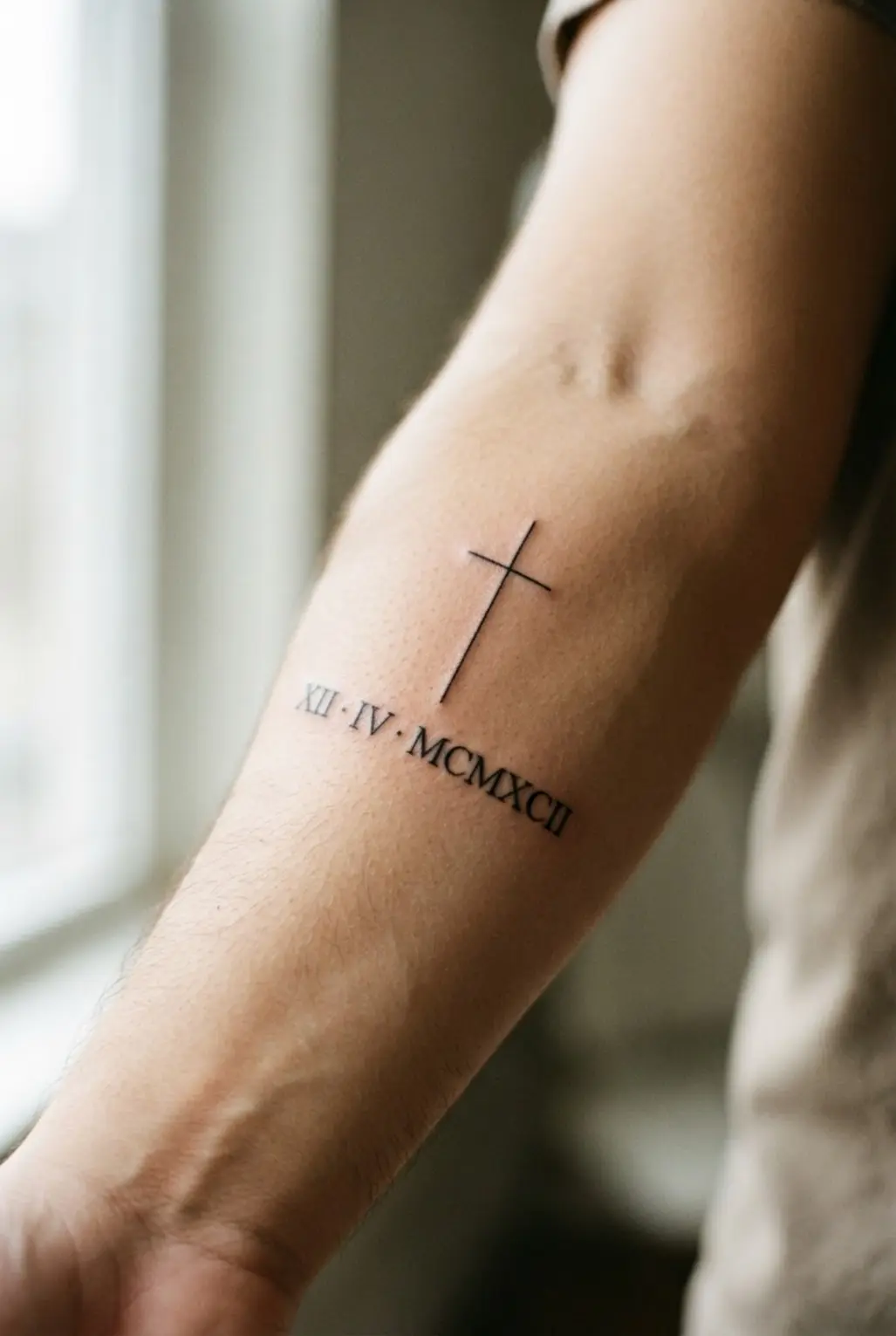 A vertical cross sits above Roman numerals on the inner forearm with a date line and crisp black lettering.