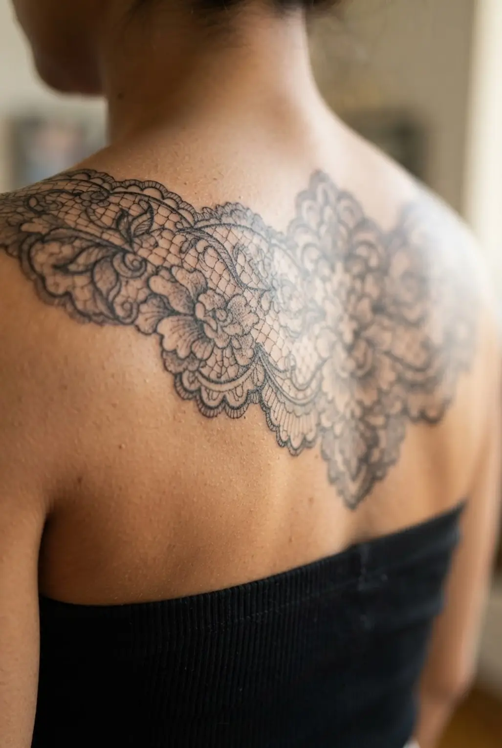 A detailed lace pattern spreads across the upper back in a graceful back tattoo for women design.