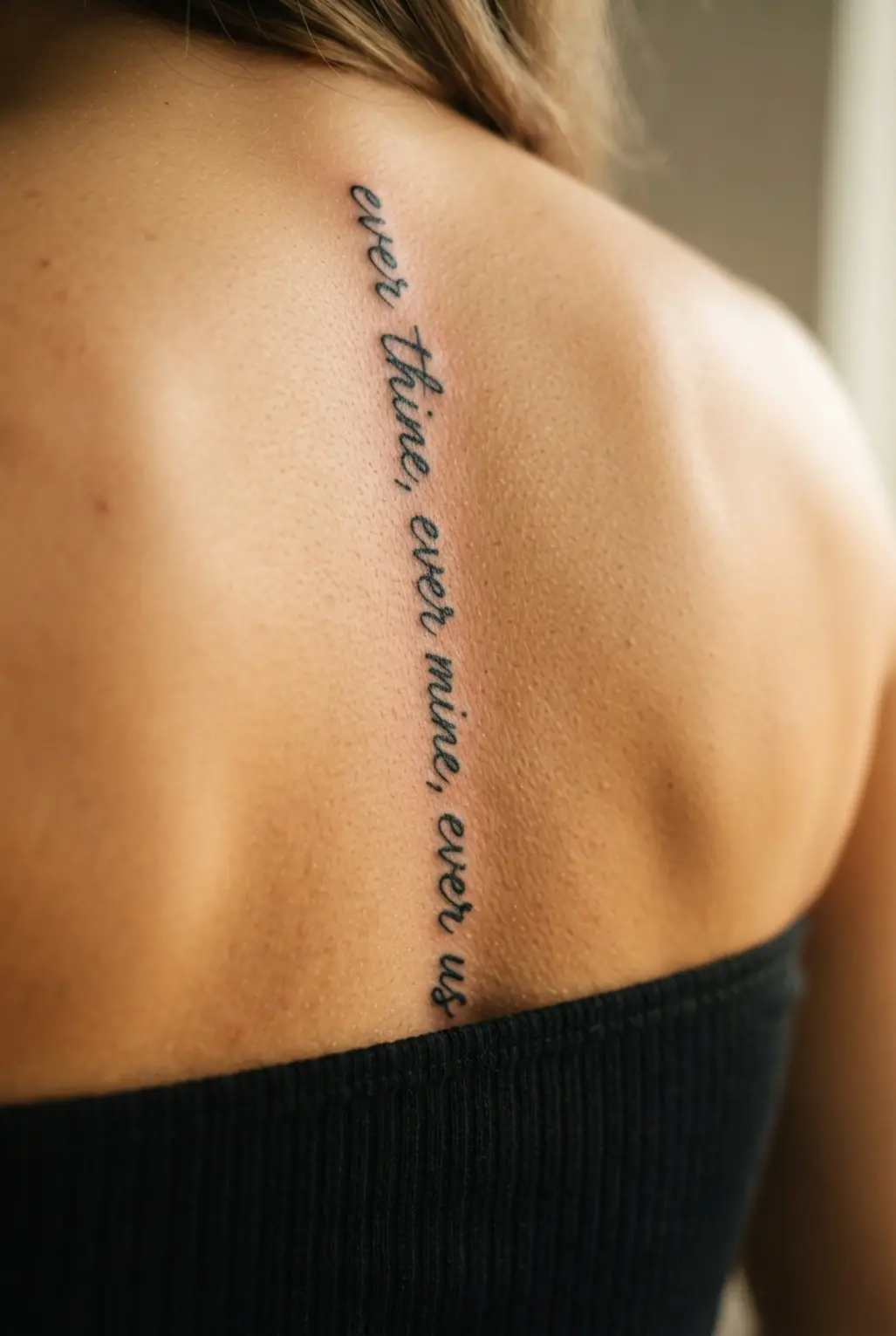 Vertical script text runs down the spine in a personal back tattoo for women design.