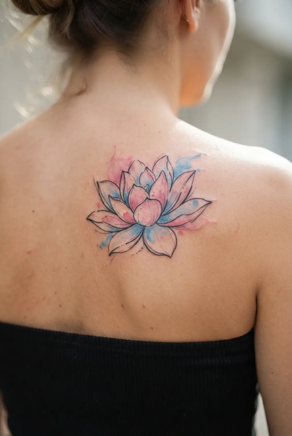 A watercolor style lotus blooms across the upper back in a colorful back tattoo for women design.