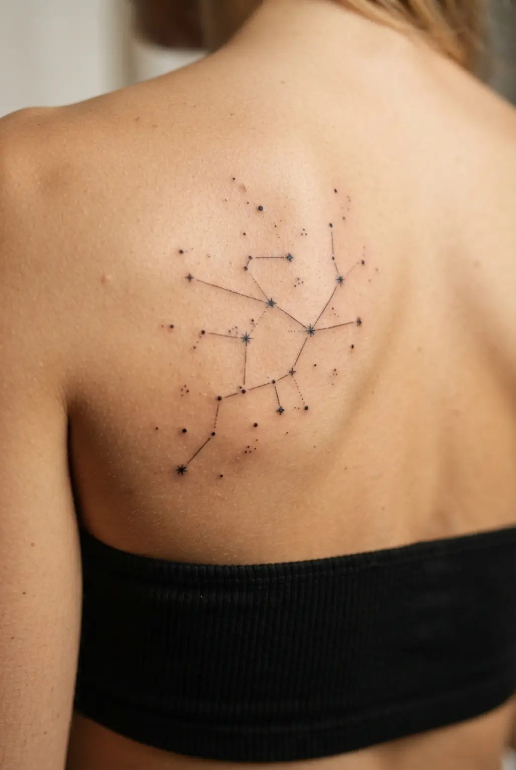 Small stars and connected dots form a tiny constellation in an upper back tattoo for women design.