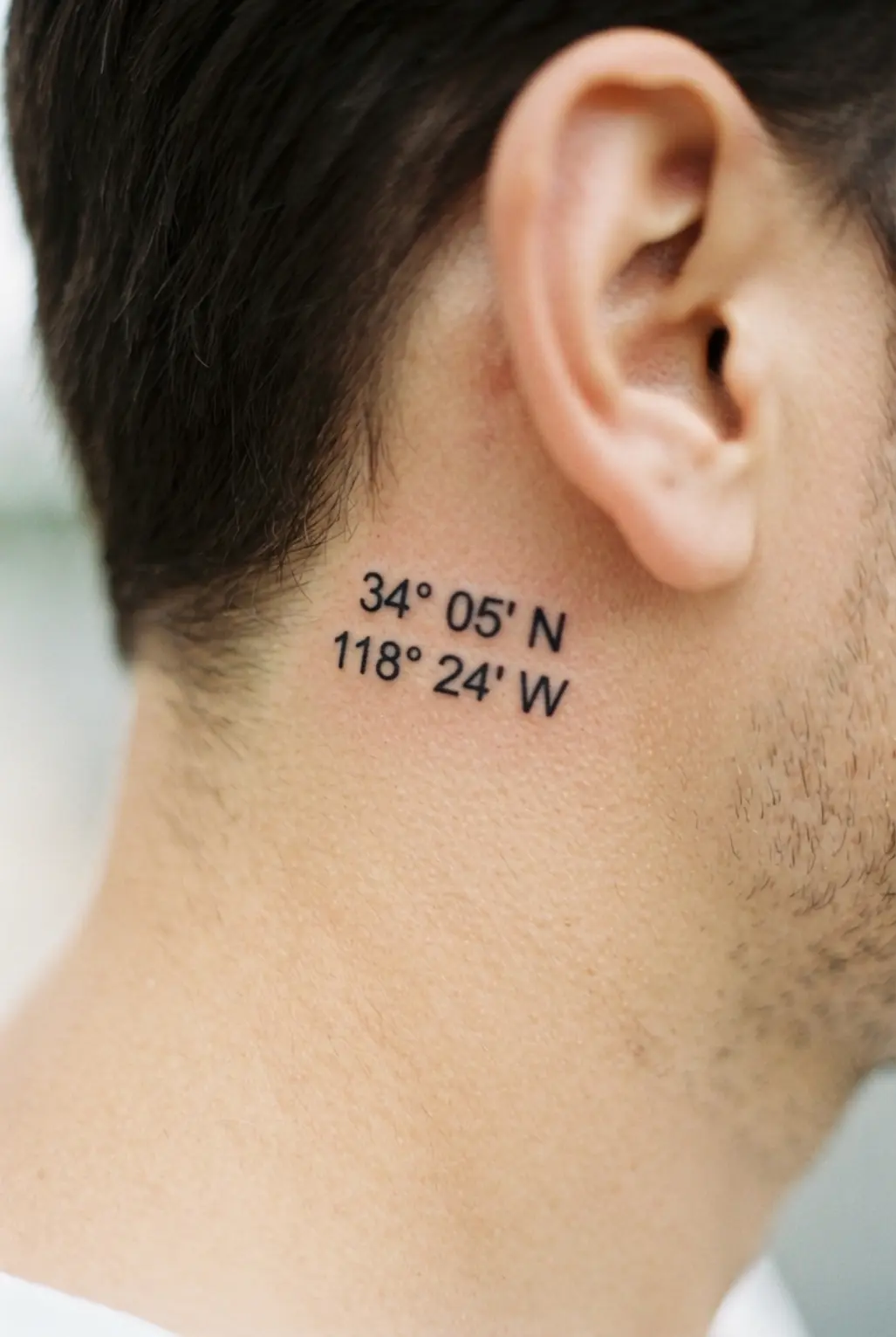 Small coordinates number sequence tattoo behind the ear, displayed in neat black numerals with compact horizontal spacing.