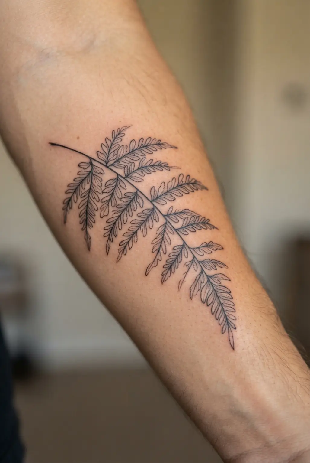 Single needle fern leaf tattoo on the forearm with a slim stem, fine leaflets, and airy black linework.