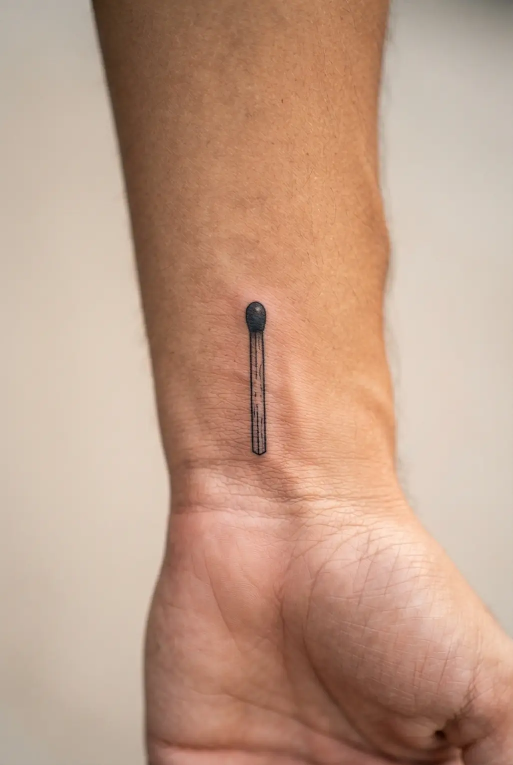 Tiny matchstick tattoo on the inner wrist with a dark tip, narrow wood lines, and a crisp black outline.
