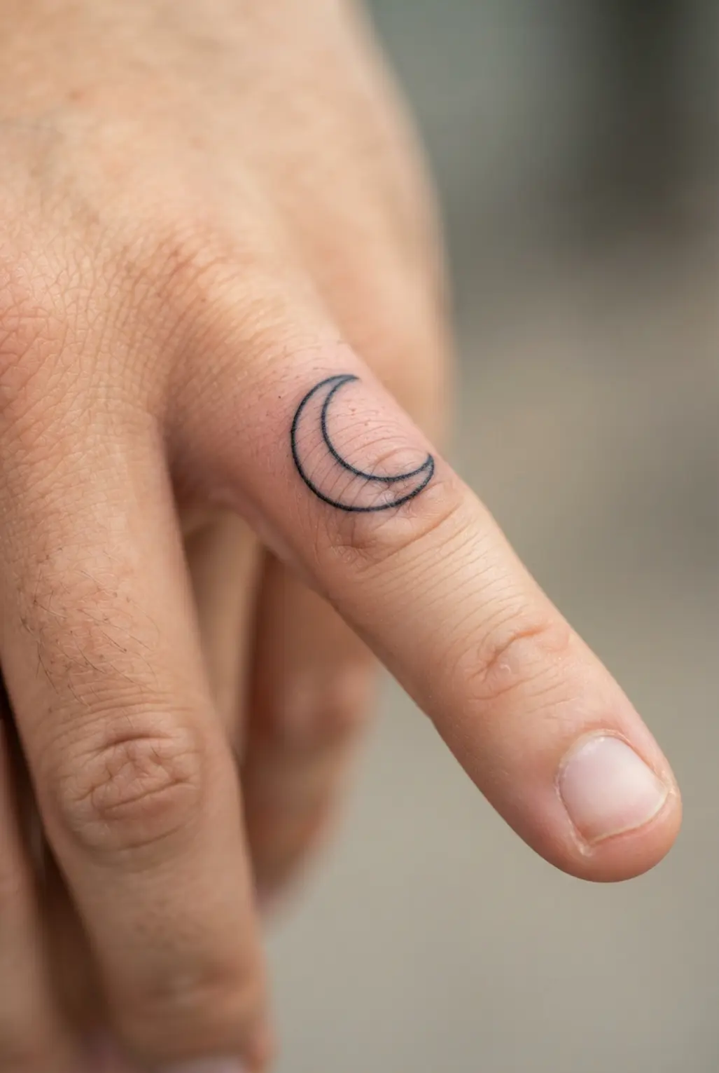 Black and white tattoo ideas showing a minimalist crescent moon on a finger with clean, narrow linework.