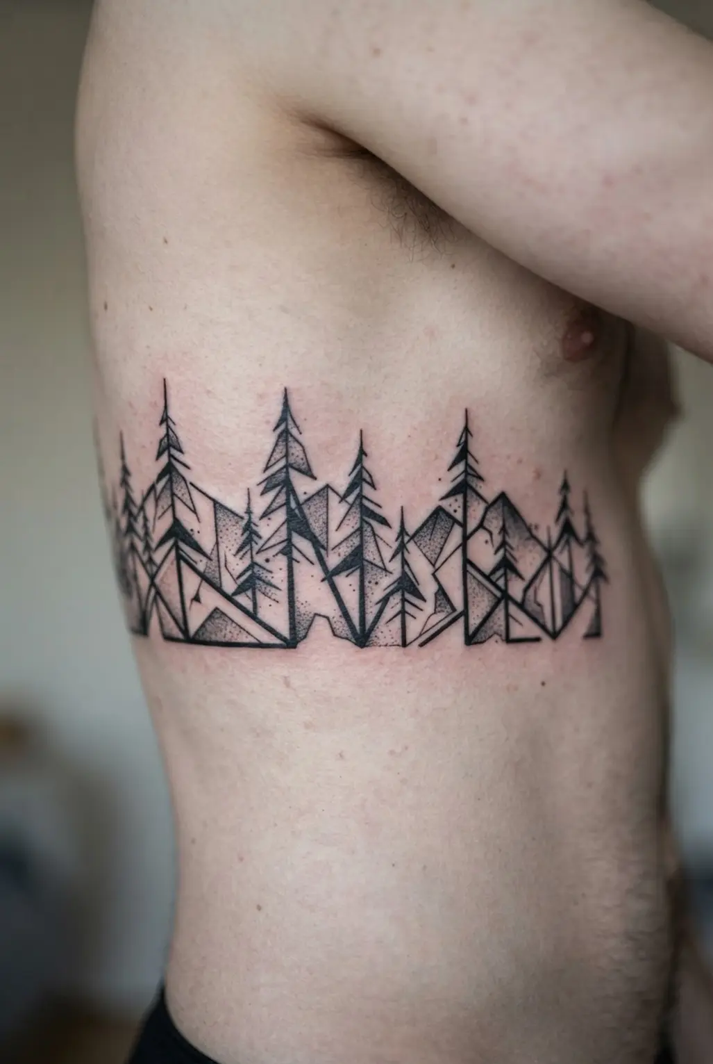 Black and white tattoo ideas featuring a geometric pine forest across the ribcage with angular trees and bold lines.