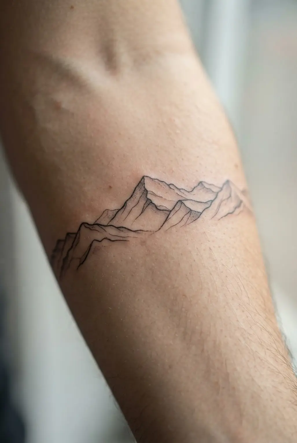 Fine-line mountain range tattoo across the forearm with distant peaks, open spacing, and thin black contours.
