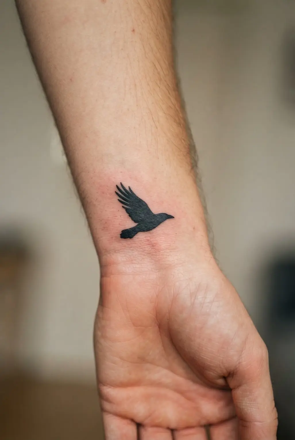 A small raven in flight appears as a clean black silhouette across the wrist with three separated feather marks.