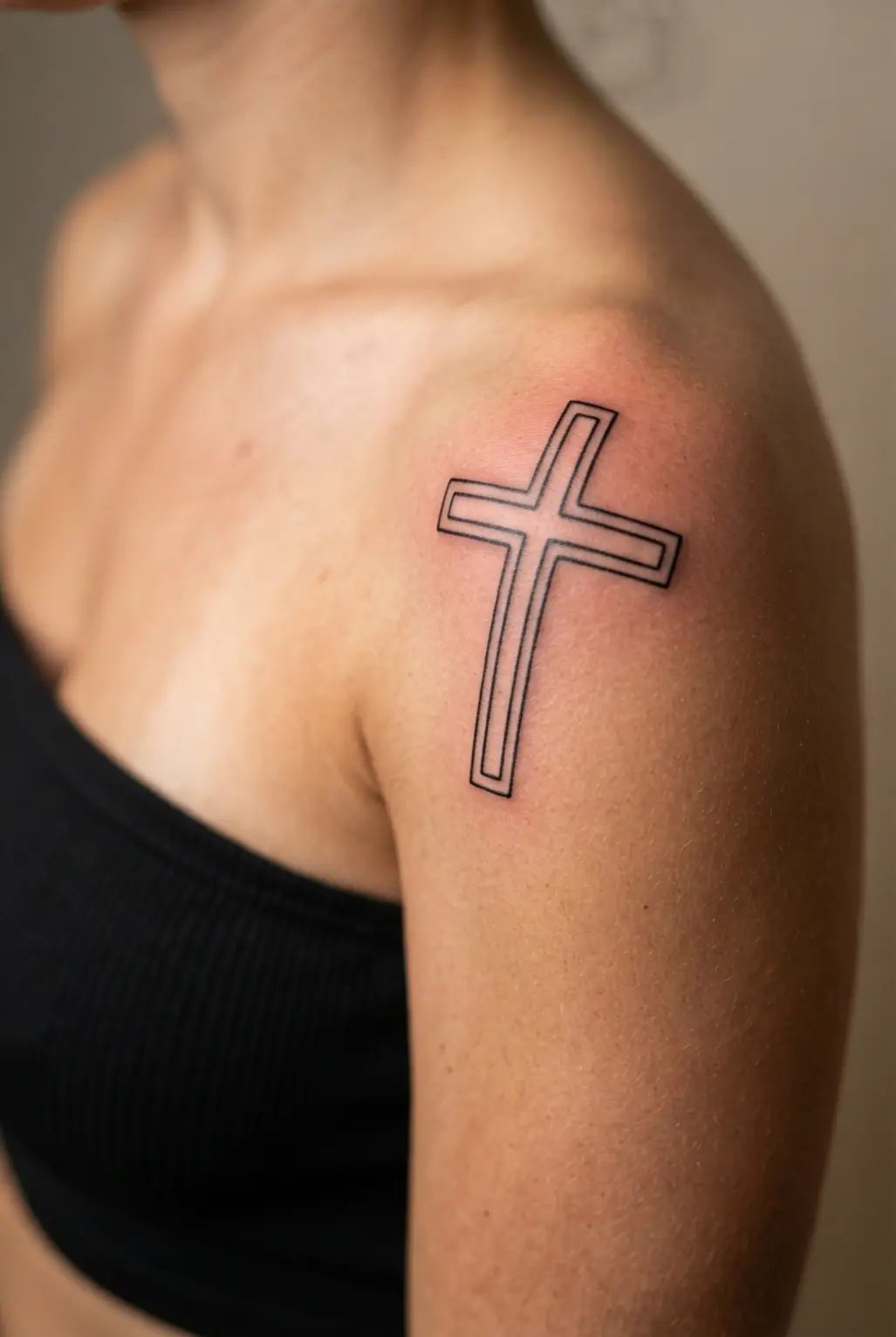 Double outline artistic cross in fine black ink with parallel borders following the curve of the shoulder.