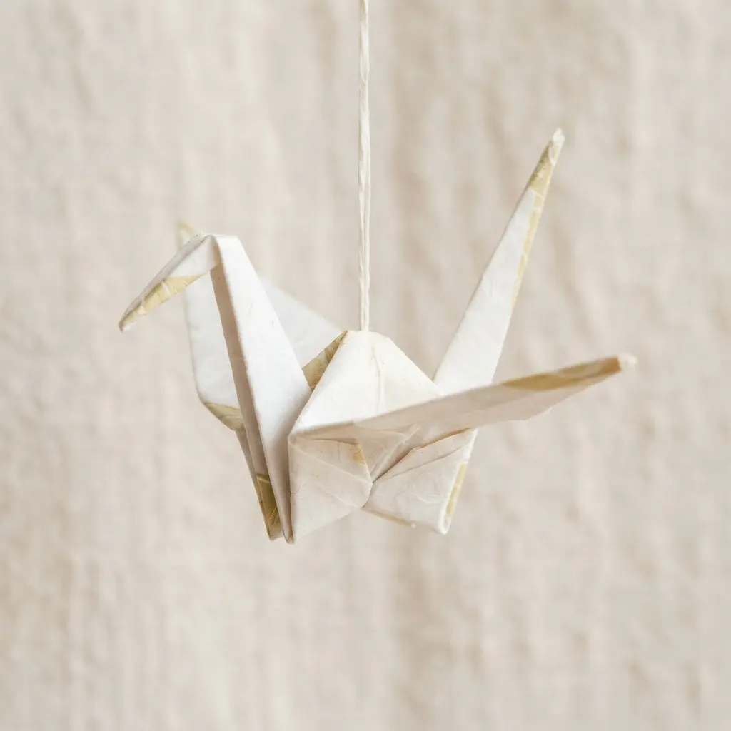 A white paper crane hangs from a thread, showing balanced wings in an easy origami project.