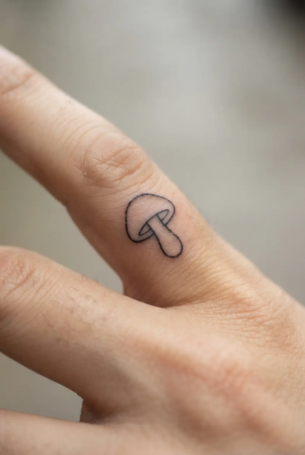 A small mushroom outline sits on a finger with a rounded cap, short stem, and open black linework.