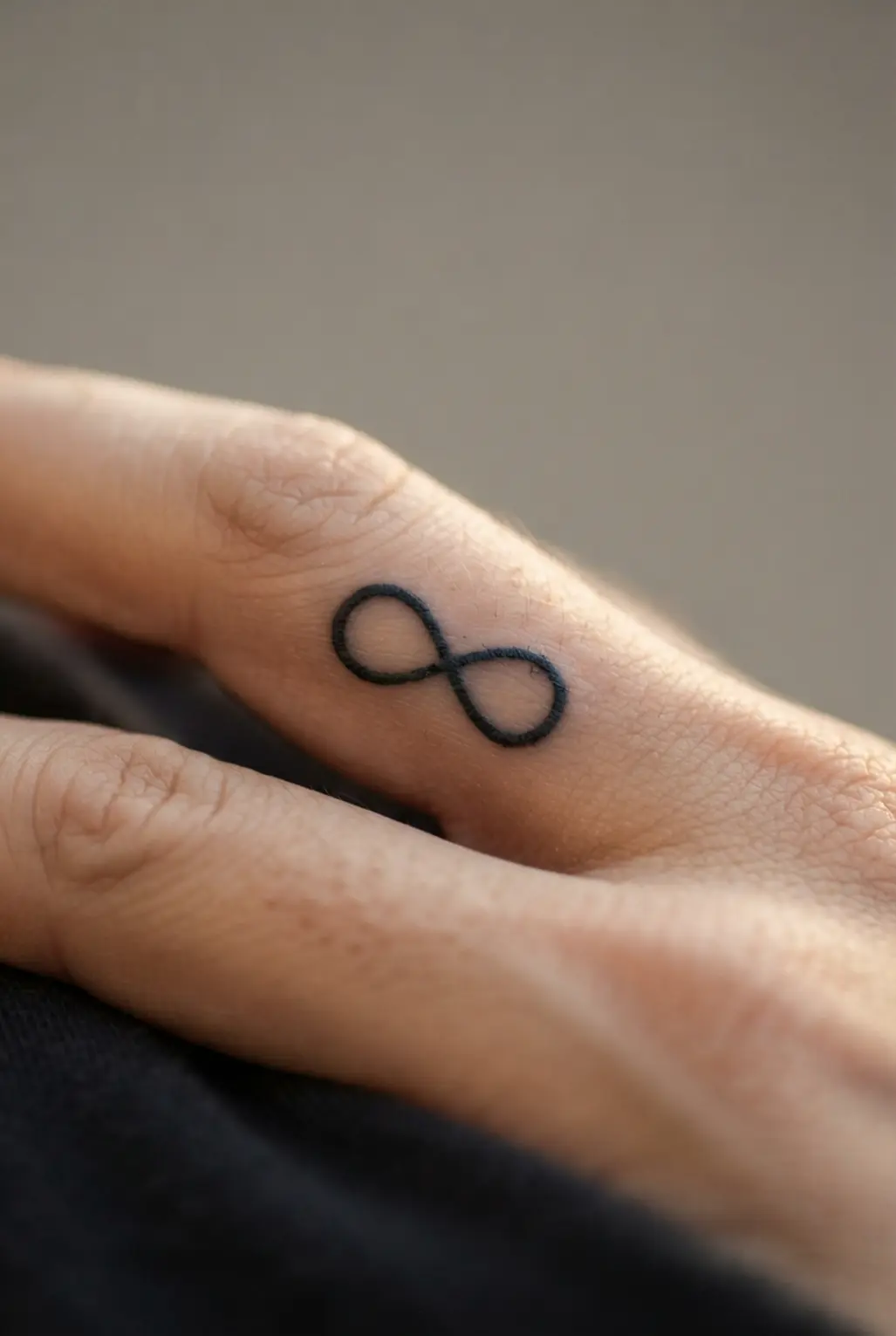 A small infinity loop crosses itself on a finger, using smooth black lines and a balanced compact shape.