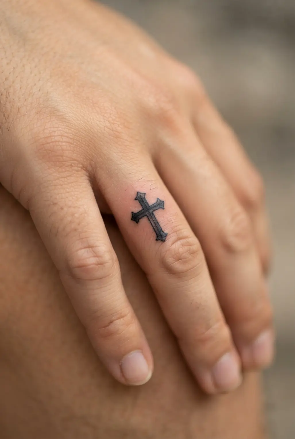 A miniature gothic cross appears on a finger with squared ends, dark lines, and a compact tiny finger tattoo form.
