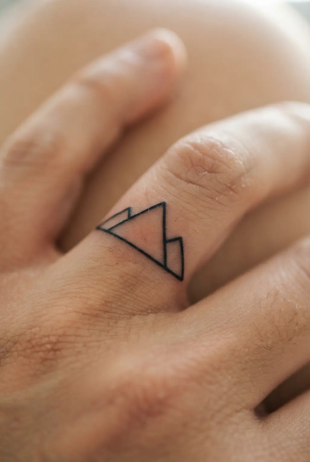 A small geometric mountain outline spans a finger, using crisp black lines and a simple triangular peak.