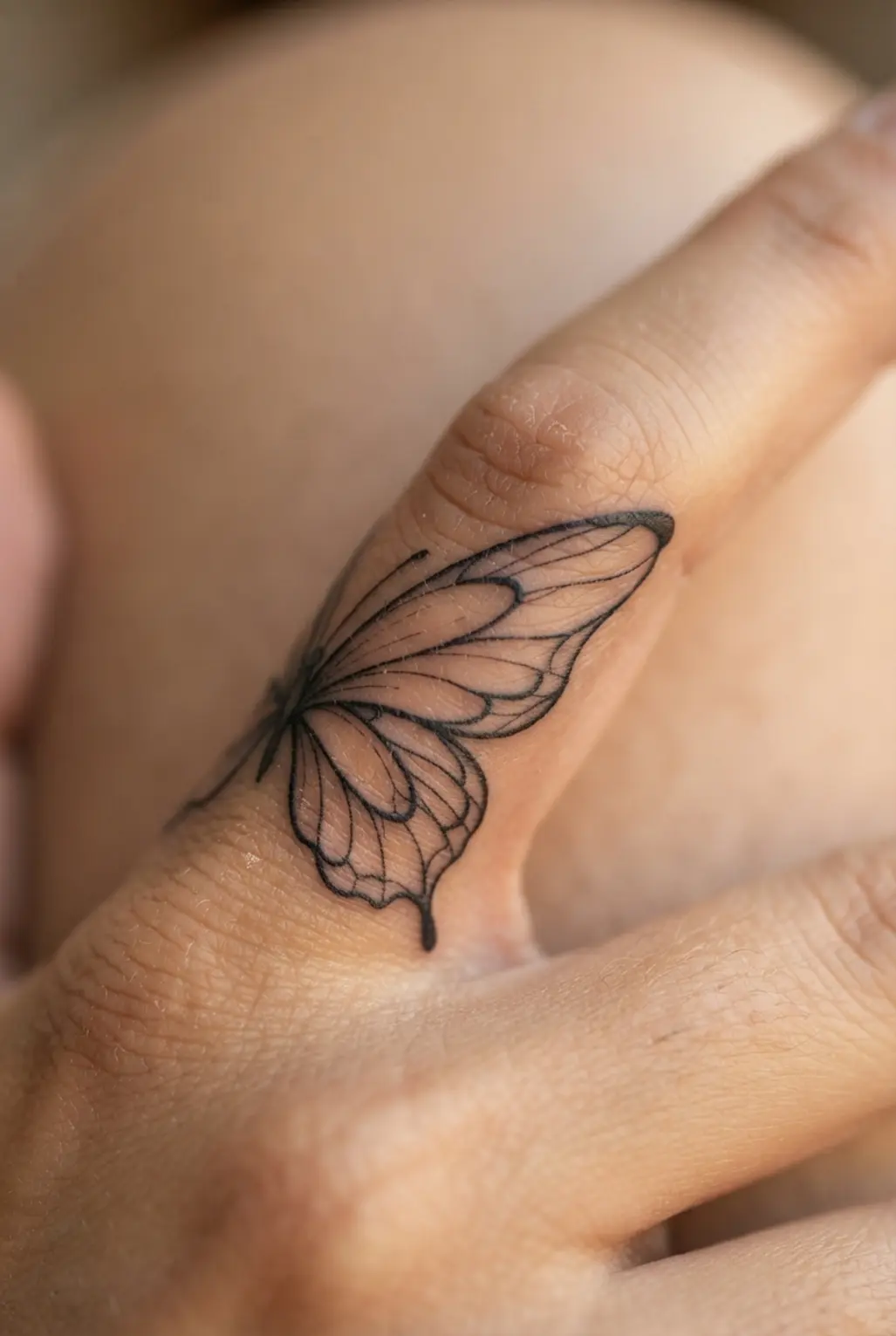 One butterfly wing curves along a finger in fine black lines, creating a light tiny finger tattoo shape.