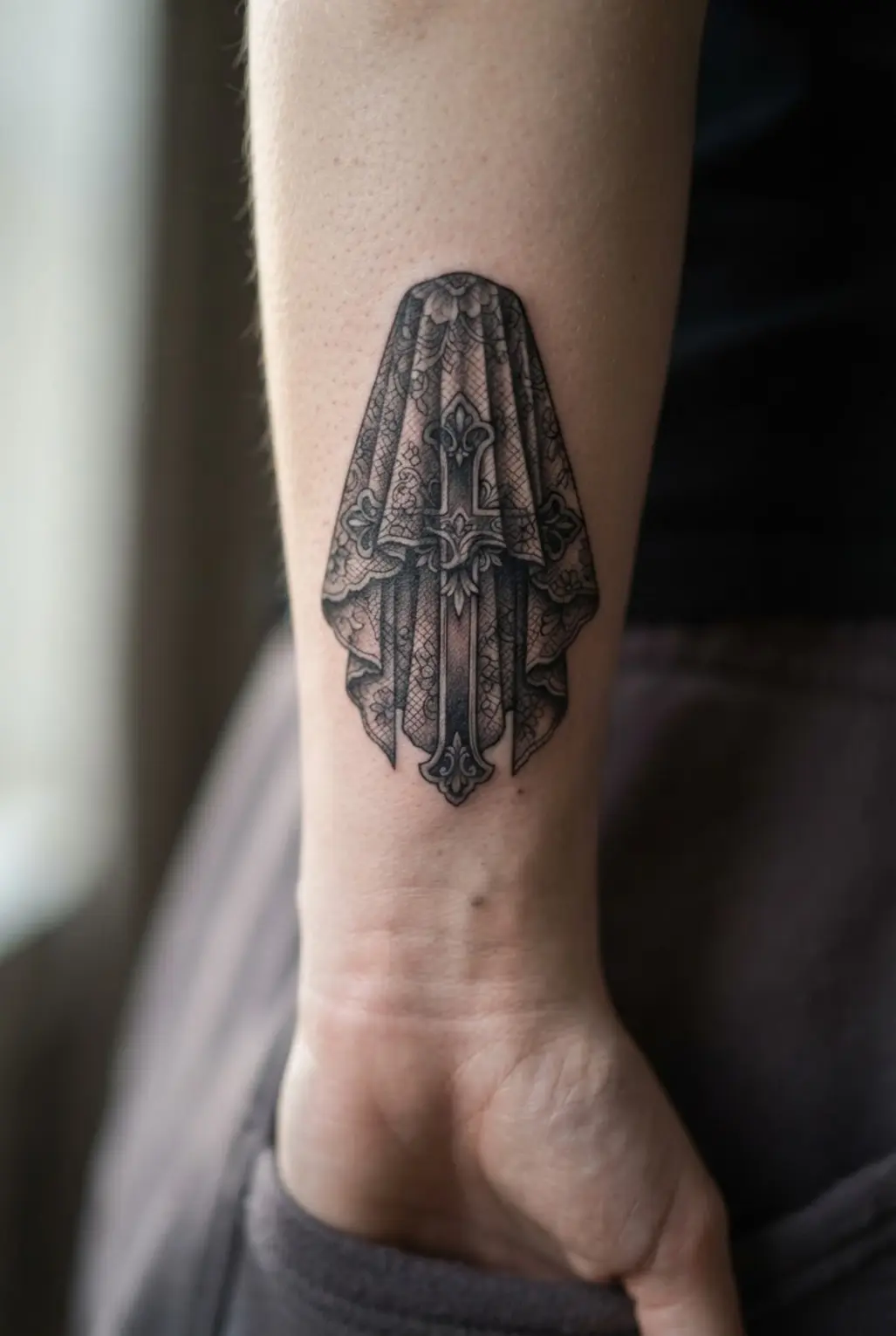 A black cross rests beneath a Victorian mourning veil with lace folds, floral trim, and soft shadowing.