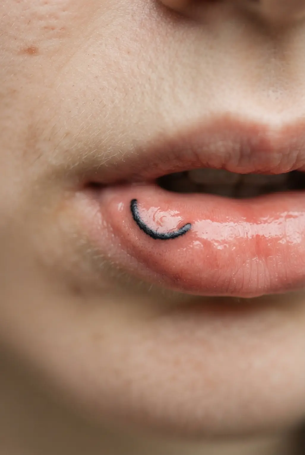 Visible comparison of small inner lip tattoo lettering, bold lines, and simple symbols in limited space.