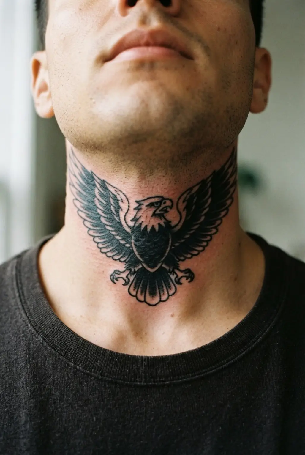 A man's neck with a classic blackwork eagle tattoo centered on the throat.