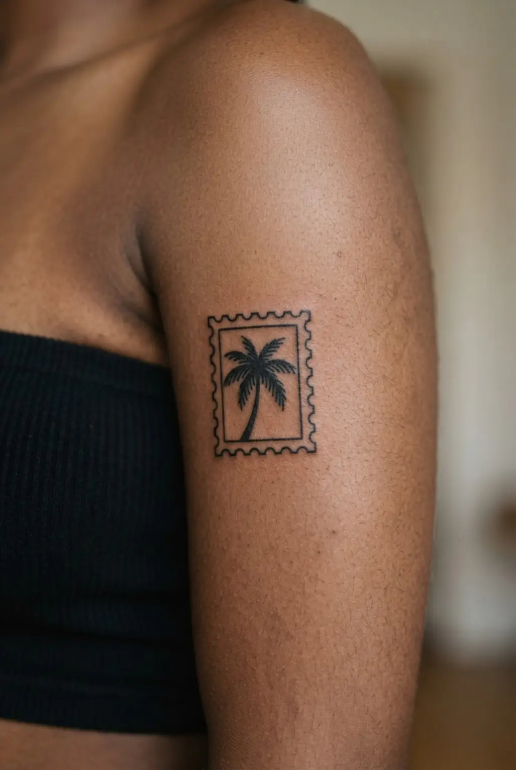 Palm tree tattoo ideas showing a small black palm inside a postage stamp frame on the bicep.