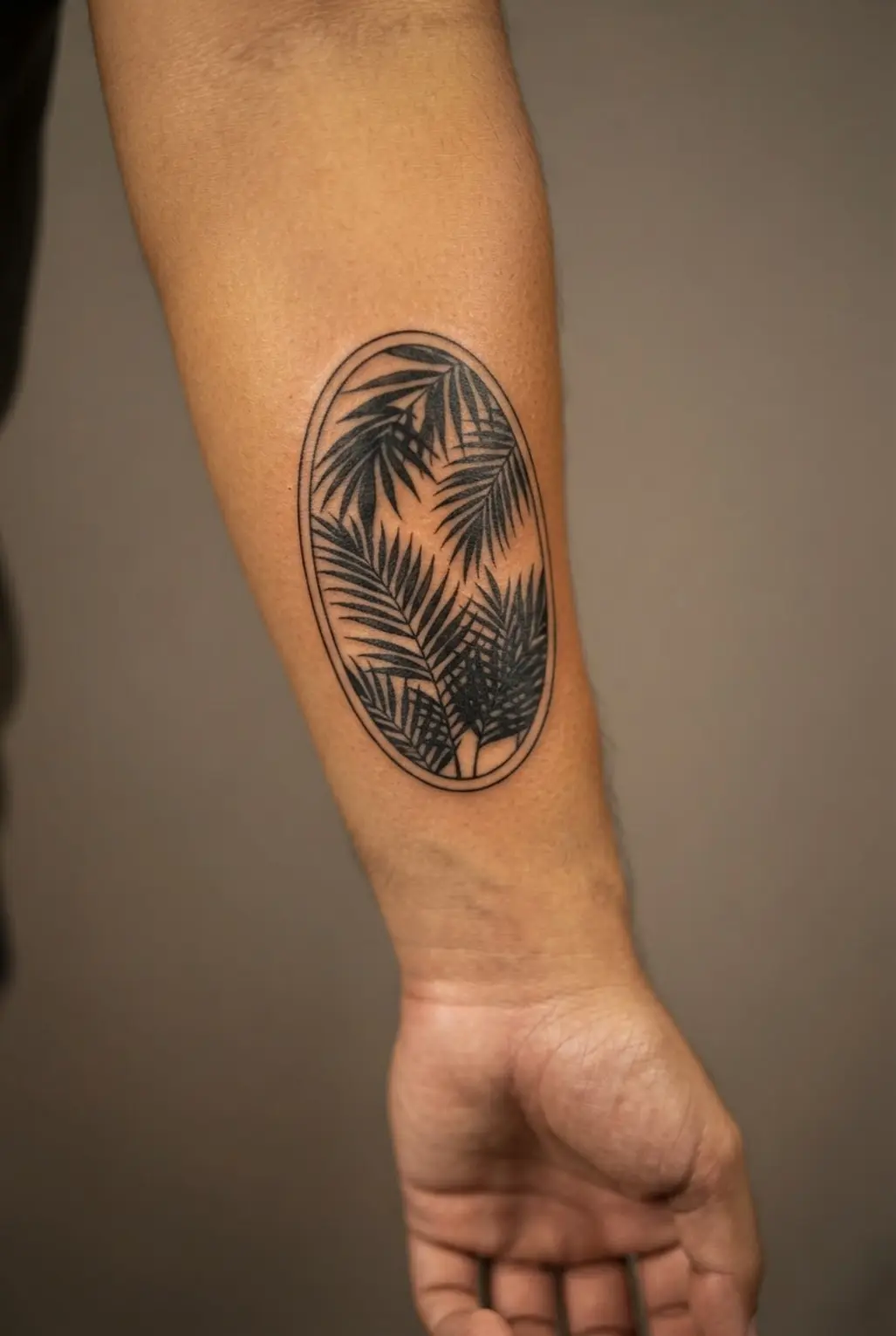 A tropical palm silhouette sits inside a slim oval frame placed vertically along the forearm.