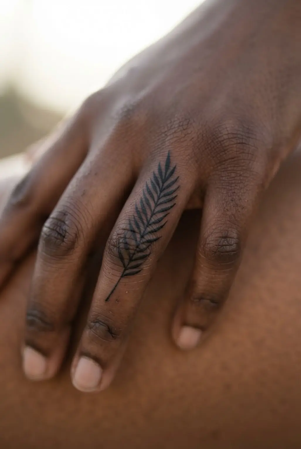 A narrow stylized palm branch follows the length of one finger in crisp black ink.